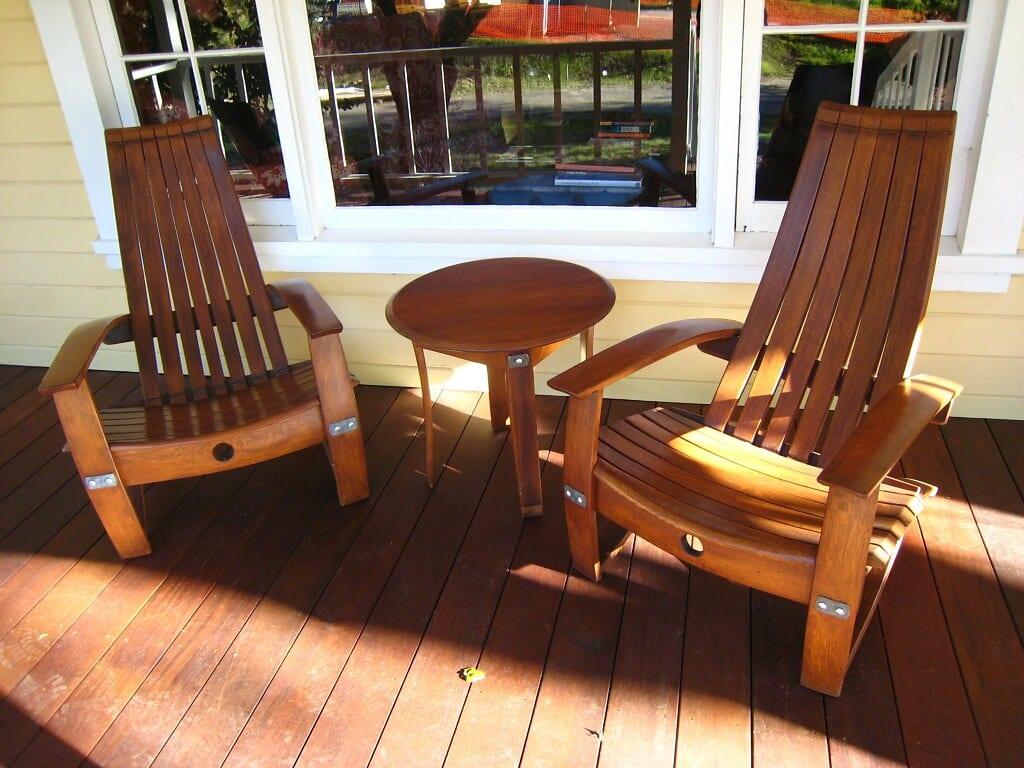 Two lounge chairs and a small round table made from the curved staves of old barrels, on a wooden deck