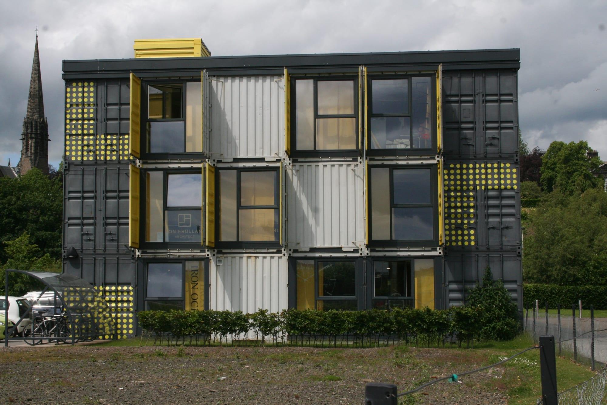 A multi-storey office building made of grey and yellow shipping containers with glazed ends