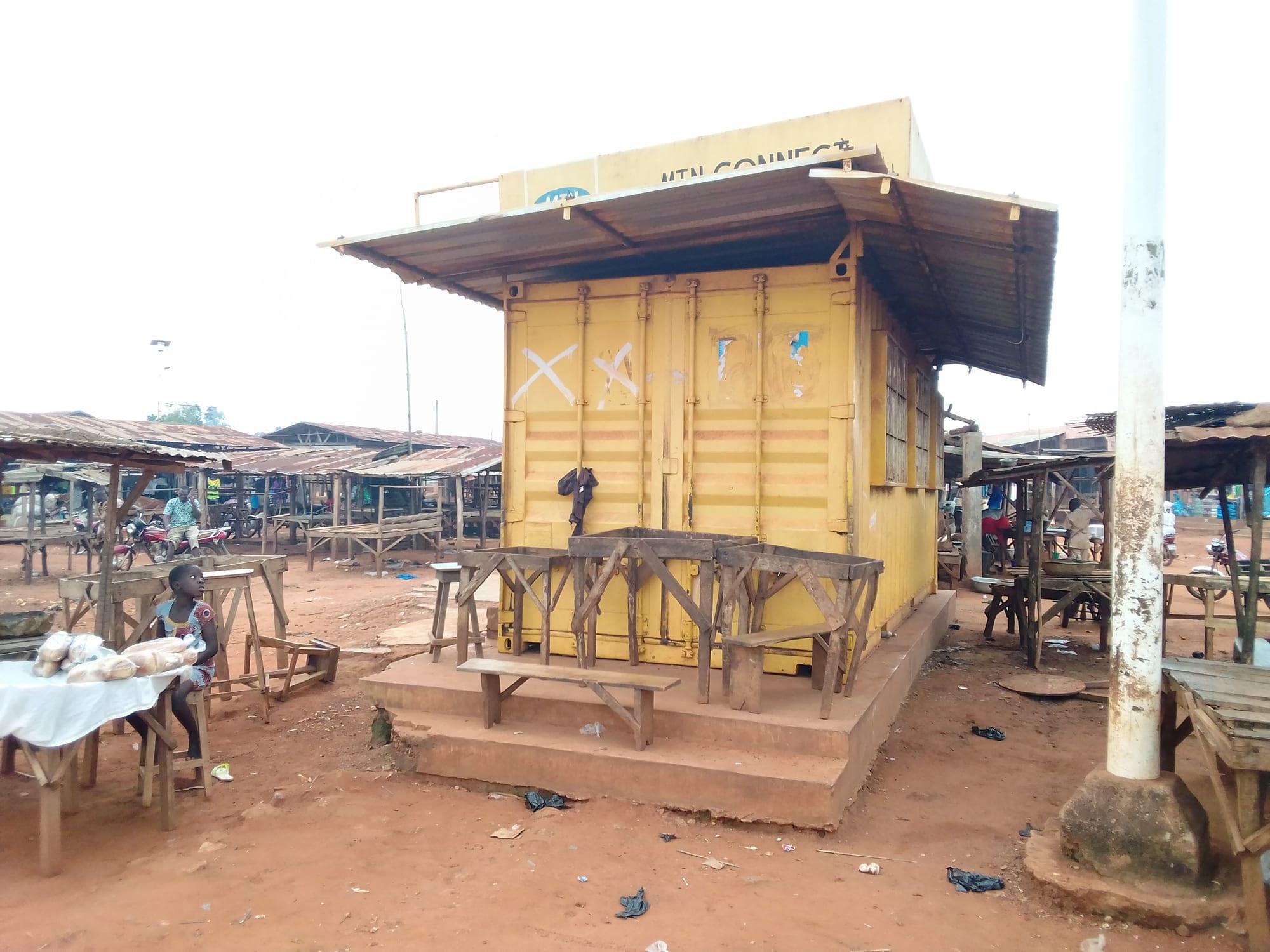 A yellow shipping container converted into a market stall with a wooden roof and tables in front