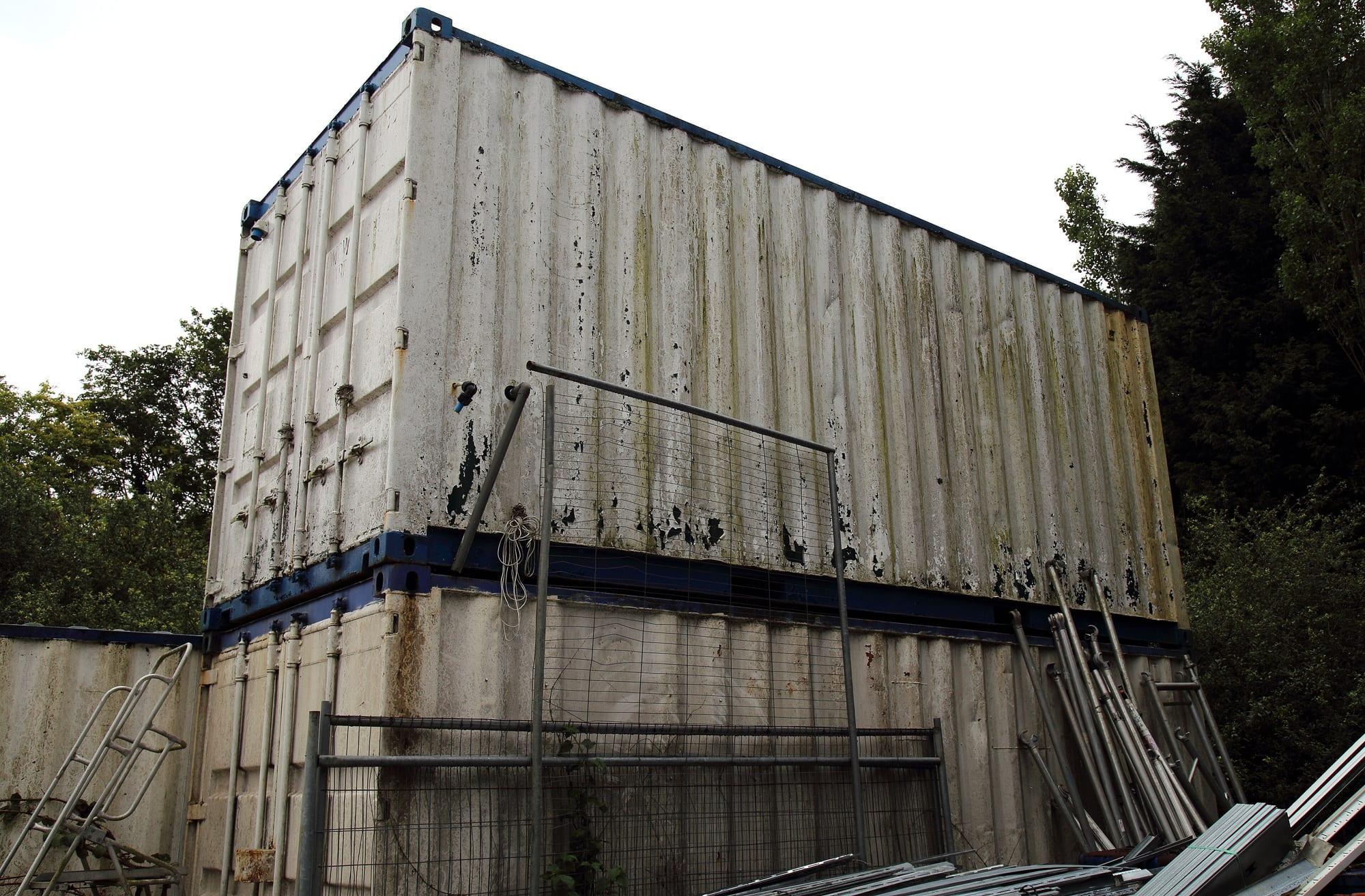 Two weathered shipping containers stacked and abandoned at the edge of a field
