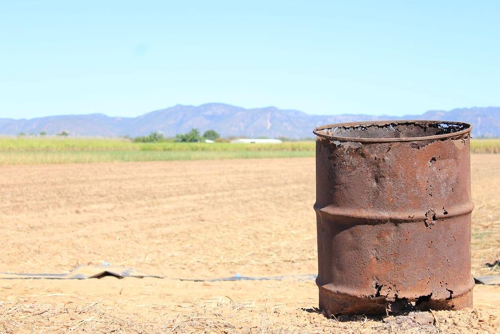 A single rusted, burnt-out oil drum standing in a bare field