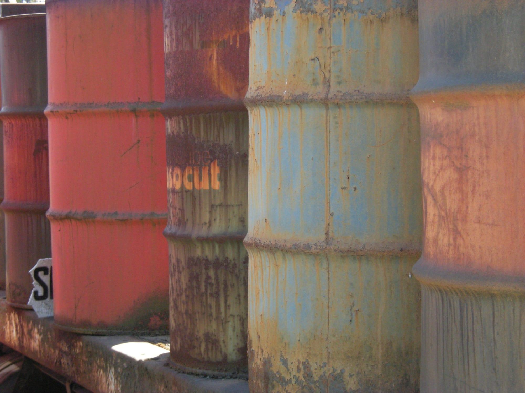 Rows of weathered red, blue and grey oil drums at a scrap-metal yard
