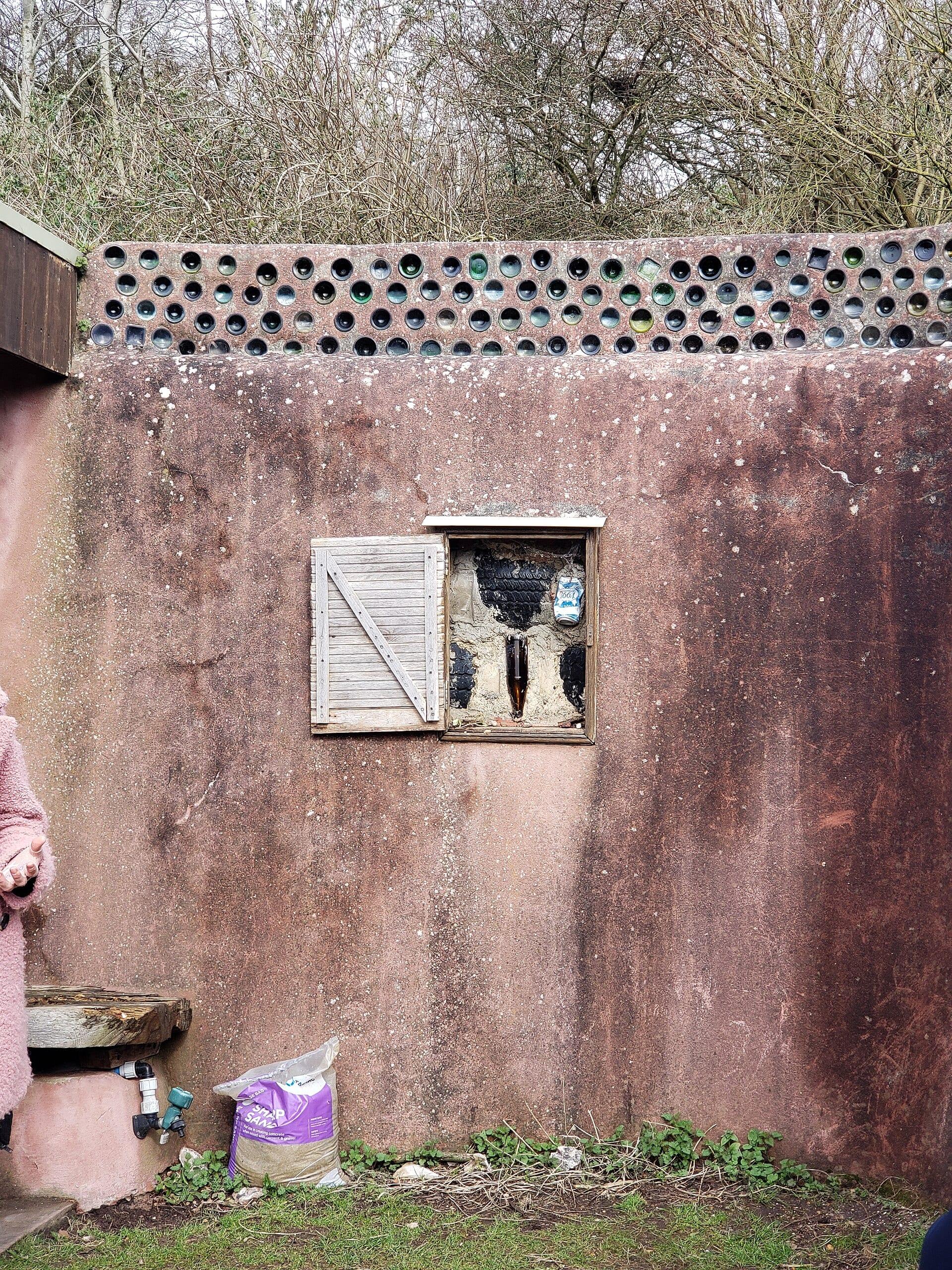 A window opened into a rendered wall reveals the car tyres, glass bottles and cans built inside it